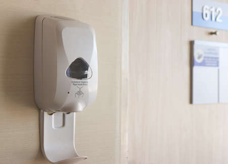 Automatic alcohol gel dispenser  on the wall at the entrance of hospital room number 612. Hand...