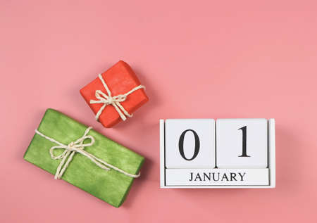 Top view of wooden calendar 01 January, red and green gift boxes on pink background. First day of the year.の写真素材