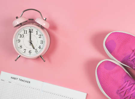 Top view or flat lay of habit tracker book, pink sneakers and pink vintage alarm clock 5 o'clock on pink background with copy space. Sports and morning routine and self development.の写真素材