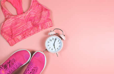 Top view or flat lay of pink sneakers, pink sport bra  and pink vintage alarm clock 5 o'clock on pink background with copy space. Sports and morning routine concept.の写真素材