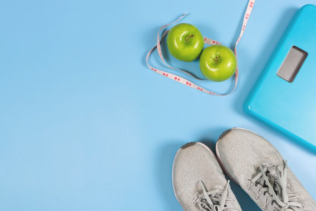 Top view or flat lay of grey sneakers ,digital weight scale, green apples and measure  tape on blue background. healthy lifestyle and weight loss concept.の写真素材