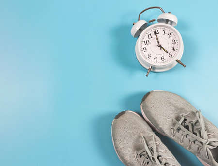 Top view or flat lay of blue  sneakers and white  vintage alarm clock 5 o'clock on blue background...