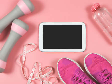 Top view or flat lay of blank screen digital tablet, pink sneakers, pink dumbbells, measuring tape and bottle of water on pink background. Online training or weight loss concept.の写真素材