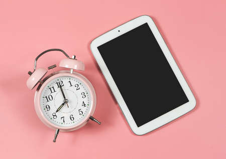 Top view or flat lay of pink vintage alarm clock and blank screen digital tablet for copy space  on...