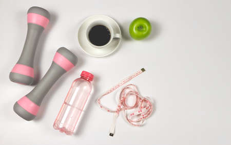 Top view or flat lay of cup of black coffee, green apple, dumbbells, bottle of water and measuring tape on white background. Healthy lifestyle and weight loss concept.の写真素材