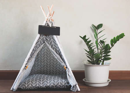 Front view of empty cloth gray pet  teepee tent with blank name tag beside plant pot on wooden floor...