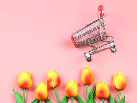 Top view or flat lay of shopping cart with yellow red tulips on pink background. Spring shopping concept.の写真素材