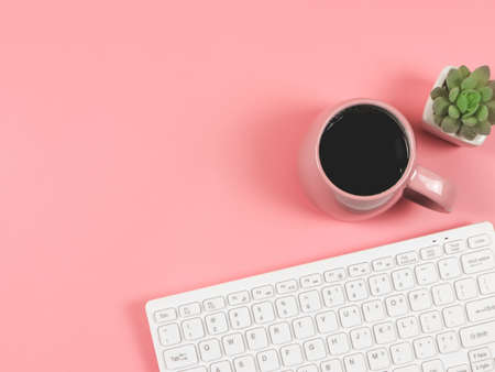 Top view or flat lay of computer keyboard, pink cup of black coffee and succulent plant pot on pink background with copy space for text. Feminine workplace. Morning routine.の写真素材