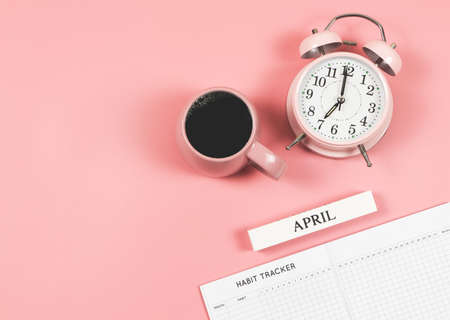 Top view or flat lay of habit tracker book, wooden calendar April, pink  vintage alarm clock 7 o'clock and pink cup of black coffee  on blue  background with copy space.の写真素材