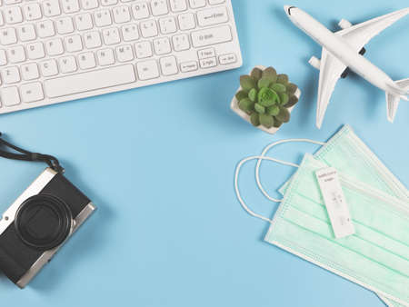 negative test result antigen test kit (ATK) on medical face masks  on blue background with computer keyboard, camera, airplane model and succulent plant pot. New normal travelling .の写真素材