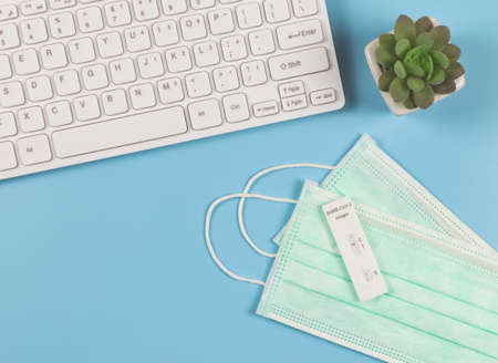 Covid-19 negative test result antigen test kit (ATK) on medical face masks  on blue background with computer keyboard and succulent plant pot. New normal workplace.の写真素材