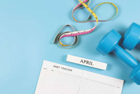 Top view or flat lay of habit tracker book, wooden calendar April, blue  dumbbells and measuring...