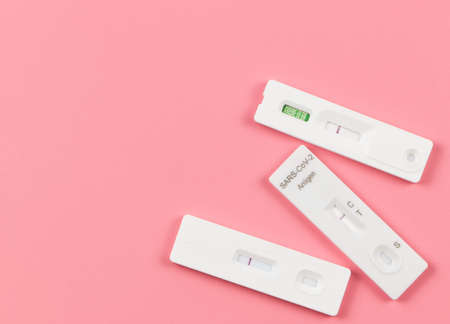 Top view or flat lay of three negative test result antigen test kits (ATK)  on pink  background with...