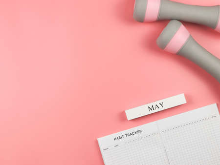 Top view or flat lay of habit tracker book, wooden calendar May,  gray pink dumbbells,  on pink background with copy space. Self development and active lifestyle concept.の写真素材