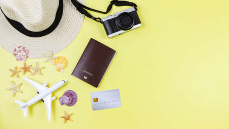 Top view or flat lay of passport, credit card, camera, straw hat, airplane model with sea shells and starfish on yellow background with copy space. Summer beach vacation background.の写真素材