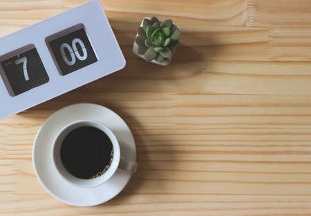Top view or flat lay of flip clock 7 am,  a cup of black coffee and succulent plant pot on wooden table background with copy space.の写真素材
