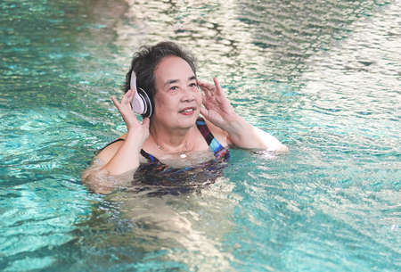 Portrait of  happy and healthy  Asian senior  woman listening to the music with headphones in a swimming pool.の写真素材