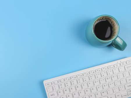 Top view or flat lay of computer keyboard, blue cup of black coffee on blue  background with copy...