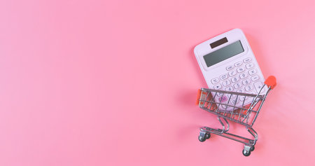 Top view or flat layout of pink calculator and  in Shopping trolley or shopping cart  on pink  background. Economic calculation of shopping.の写真素材