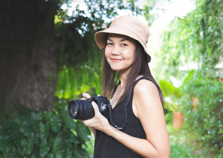 Portrait of Asian woman, wearing hat and black top sleeveless, standing in the garden and  holding...