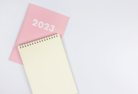 Top view or flat lay of blank paper note book on pink diary 2023 on white background.