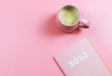 Top view or flat lay of pink 2023 diary or planner with pink cup of coffee on pink background. New...