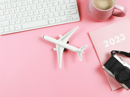Top view or flat lay of computer keyboard, pink cup of coffee, airplane model, 2023 diary or planner...