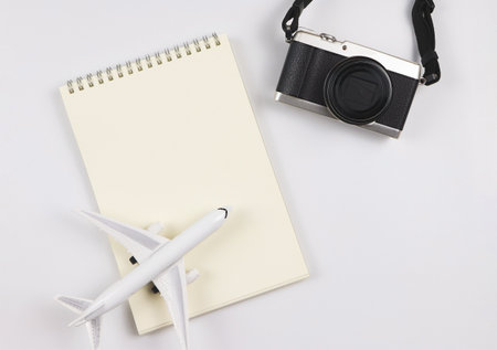 Top view or flat lay of blank page opened notebook, airplane model  and camera on white  background with copy space. Travel, photo and memory concept.の写真素材