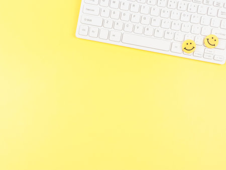 Top view or flat lay of  two yellow circle smiling faces on white computer keyboard on yellow ...