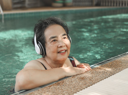 Portrait of  happy and healthy  Asian senior  woman listening to the music with headphones in a poolの写真素材
