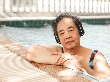 Portrait of  happy and healthy  Asian senior  woman listening to the music with headphones in a poolの写真素材