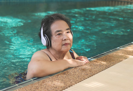 Portrait of  happy and healthy  Asian senior  woman listening to the music with headphones in a poolの写真素材