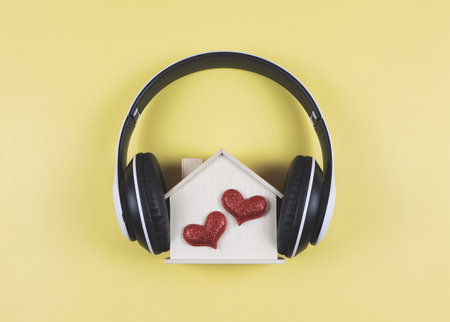 Top view or flat lay of wooden model house with two red glitter hearts covered with headphones isolated on yellow background. music or podcast, home of love, valentines.の写真素材