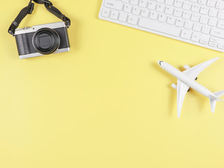 Top view or flat lay of airplane model, computer keyboard, and digital camera with copy space on yellow background, business and traveling concept.の写真素材