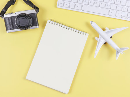 Top view or flat lay of airplane model, computer keyboard, opened blank page notebook and digital camera with copy space on yellow background, business and traveling concept.の写真素材