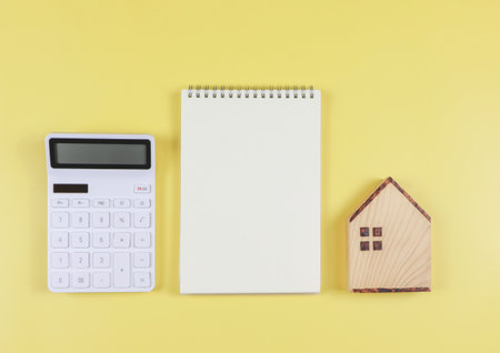 Top view or flat layout of wooden house model, white calculator, blank page opened  notebook  on yellow  background with copy space, home purchase concept.の写真素材