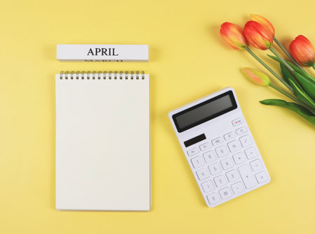 Top view or flat layout of opened blank page notebook with wooden calendar April, white calculator and tulips on yellow background. monthly financial plan concept.の写真素材