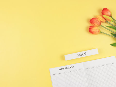 Top view or flat layout of Habit tracker book, wooden calendar May,  and tulips on yellow background with copy space.の写真素材