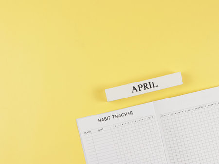 Top view or flat layout of Habit tracker book, wooden calendar April  on yellow background with copy space.の写真素材