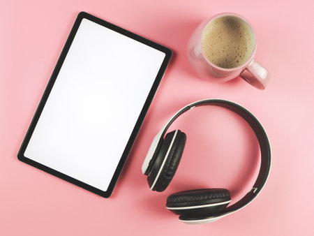 Top view of flat lay of white blank screen digital tablet, pink cup of coffee and headphones isolated on pink backgroundの写真素材