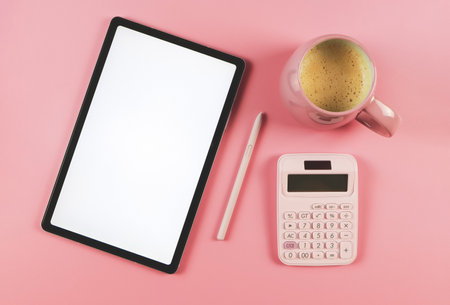 Top view or flat lay of digital tablet with blank white screen, pink stylus pen,  pink cup of...