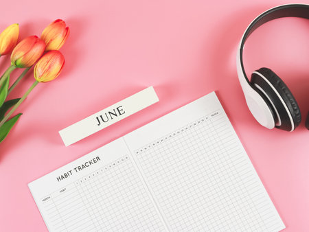 Top view or flat lay of habit tracker book with wooden calendar June,  headphones and tulips  on pink background.の写真素材