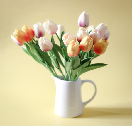 Front view of colorful tulips in a white vintage ceramic jar on yellow background.の写真素材