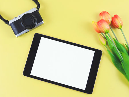 Top view or flat lay of digital tablet with blank white screen, tuip flowers  and digital camera isolated on yellow background.の写真素材
