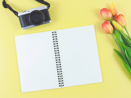 Top view or flat lay of blank page opened notebook, digital camera and red yellow tulips flowers on yellow background with copy space.の写真素材