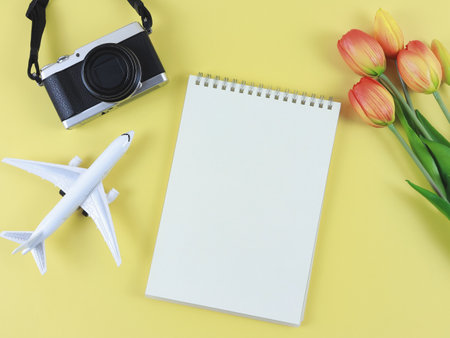 Top view or flat lay of blank page opened notebook, airplane model, digital camera and tulips flowers  on yellow  background with copy space.の写真素材