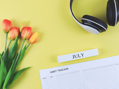 Top view or flat lay of habit tracker book with wooden calendar July,  headphones and tulips  on yellow background.の写真素材