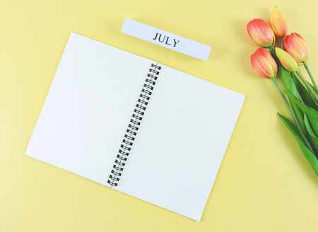 Top view or flat lay of opened blank pages notebook or diary, wooden calendar July with tulips...