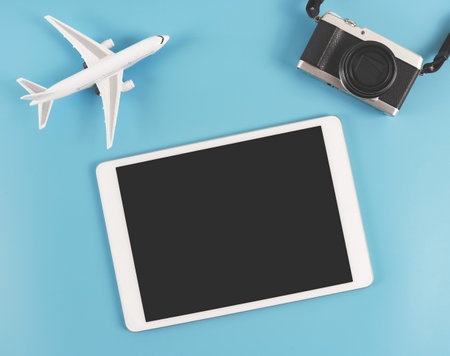 Top view or flat lay of digital tablet with blank black  screen, digital camera and  airplane model  isolated on blue background. travel planning concept.の写真素材