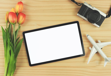 Top view or flat lay of digital tablet with blank white screen, tulip flowers, airplane model and  digital camera isolated on wooden table background.の写真素材